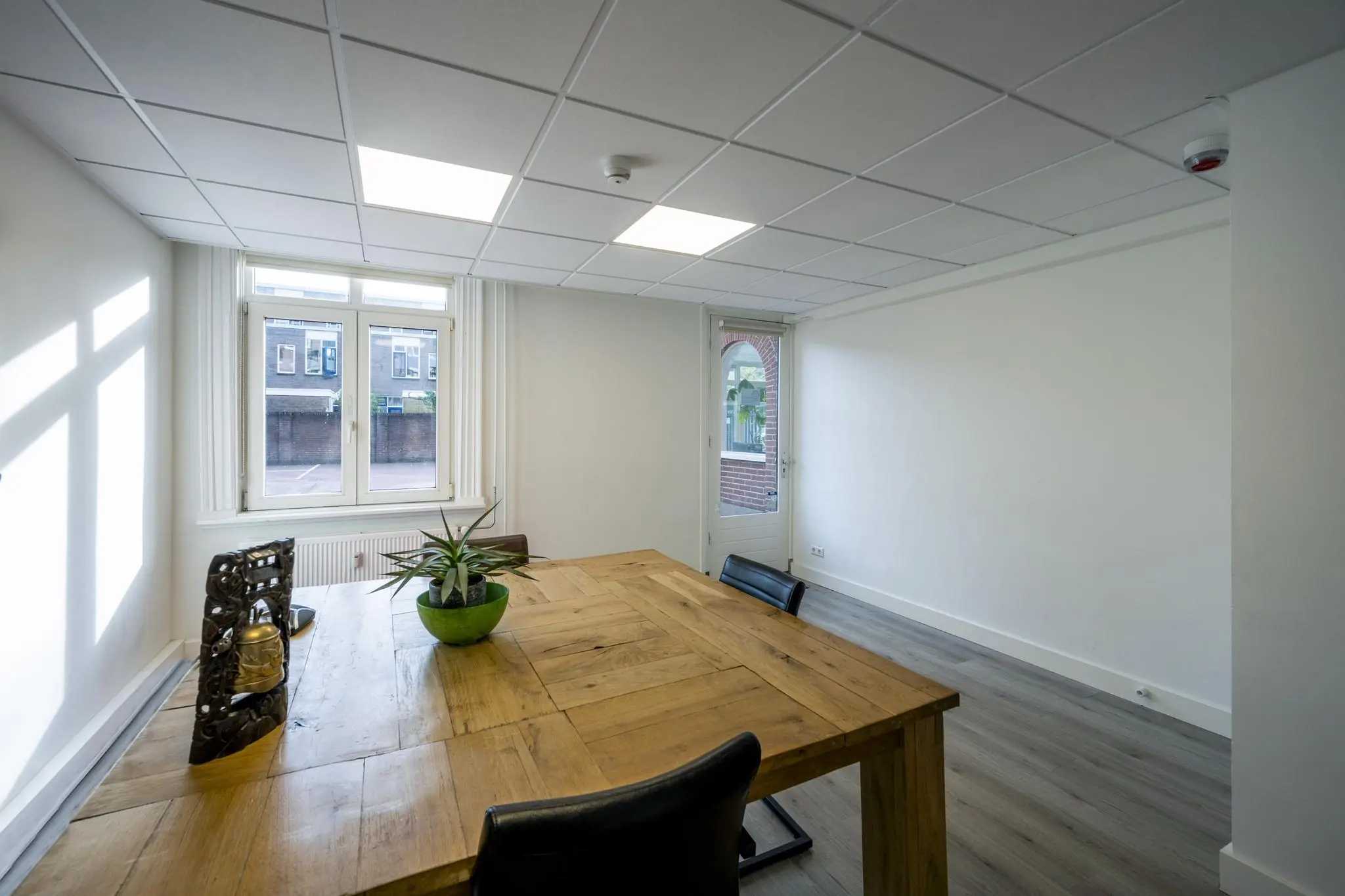 Vergaderruimte met houten tafel, enkele stoelen en zicht op de Nieuwe Gracht door het raam.